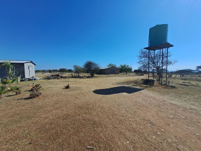A wide view of the farm grounds featuring a raised water tank on a metal stand and a small outbuilding in the distance.
