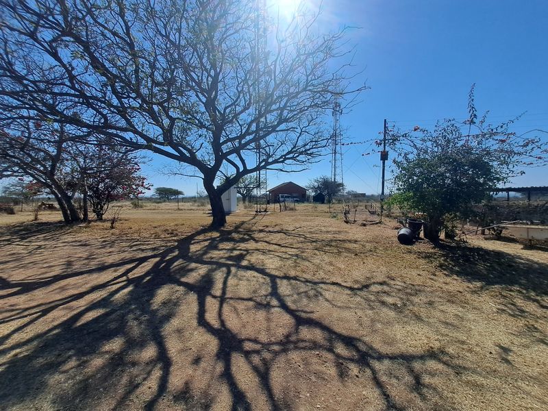 A wide-angle view of the farm grounds featuring mature trees, open dry land, and a telecommunications tower in the distance.