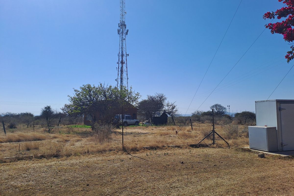 A wide view of the farm grounds featuring a large telecommunications tower, utility infrastructure, and open dry landscape.