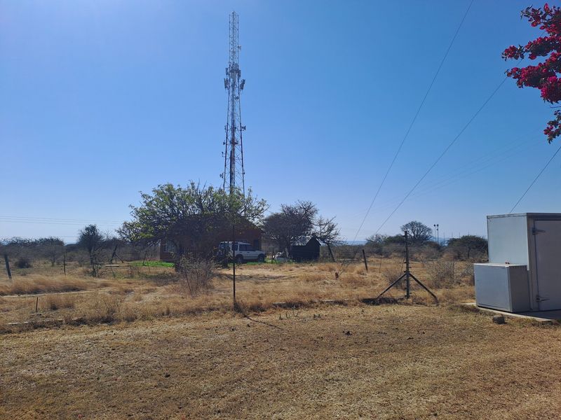 A wide view of the farm grounds featuring a large telecommunications tower, utility infrastructure, and open dry landscape.
