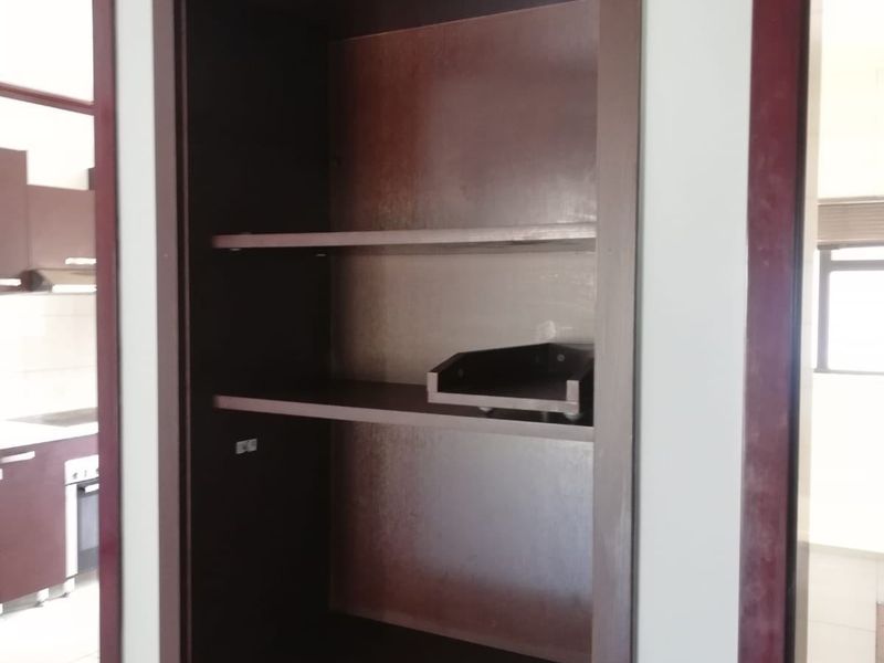 A built-in dark wood shelving unit located in a hallway, providing integrated storage space with visible electrical points.
