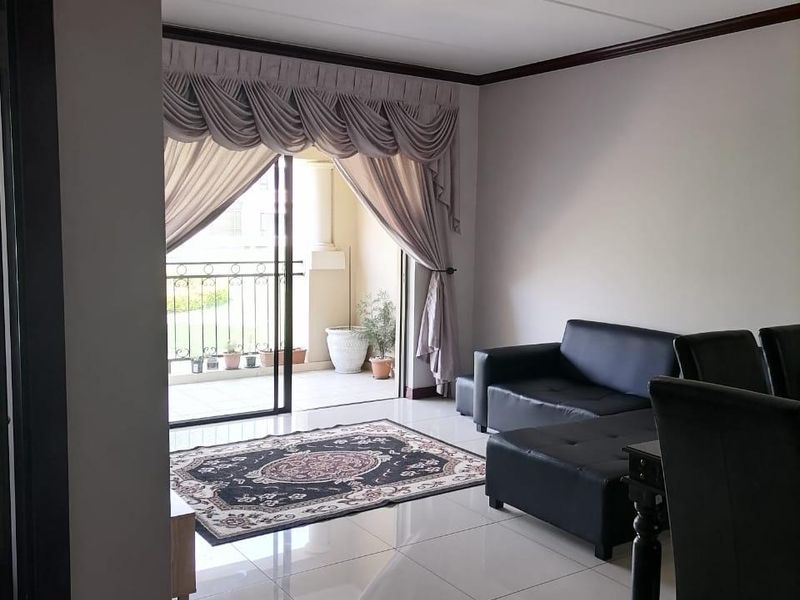 A bright living room featuring tiled flooring and direct access to a private balcony through a sliding glass door.