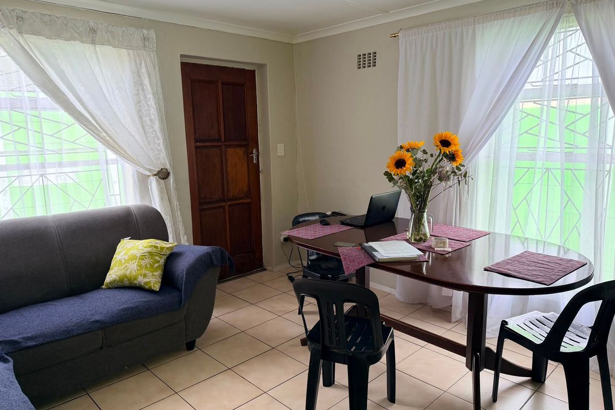 A functional living area featuring ceramic floor tiles, a timber door, and large windows fitted with security bars.