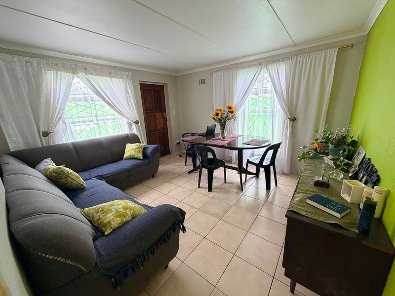 Open plan living and dining area featuring tiled flooring, security bars on windows, and a timber entrance door.
