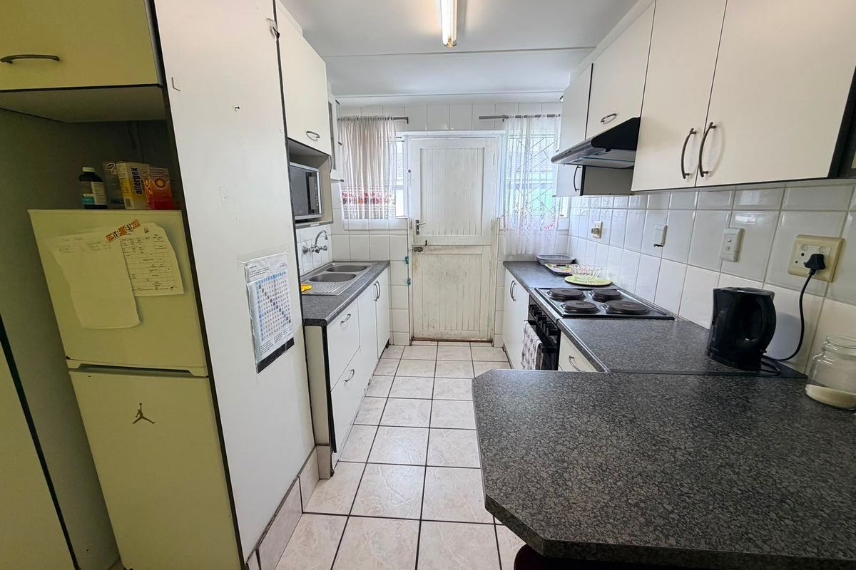 A functional galley-style kitchen featuring white cabinetry, dark laminate countertops, tiled flooring, and a built-in electric hob with an extractor fan.