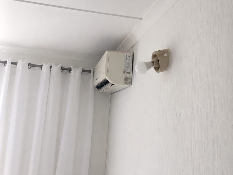 A corner view showing a wall-mounted air conditioning unit and an exposed light bulb fixture on a white textured wall.