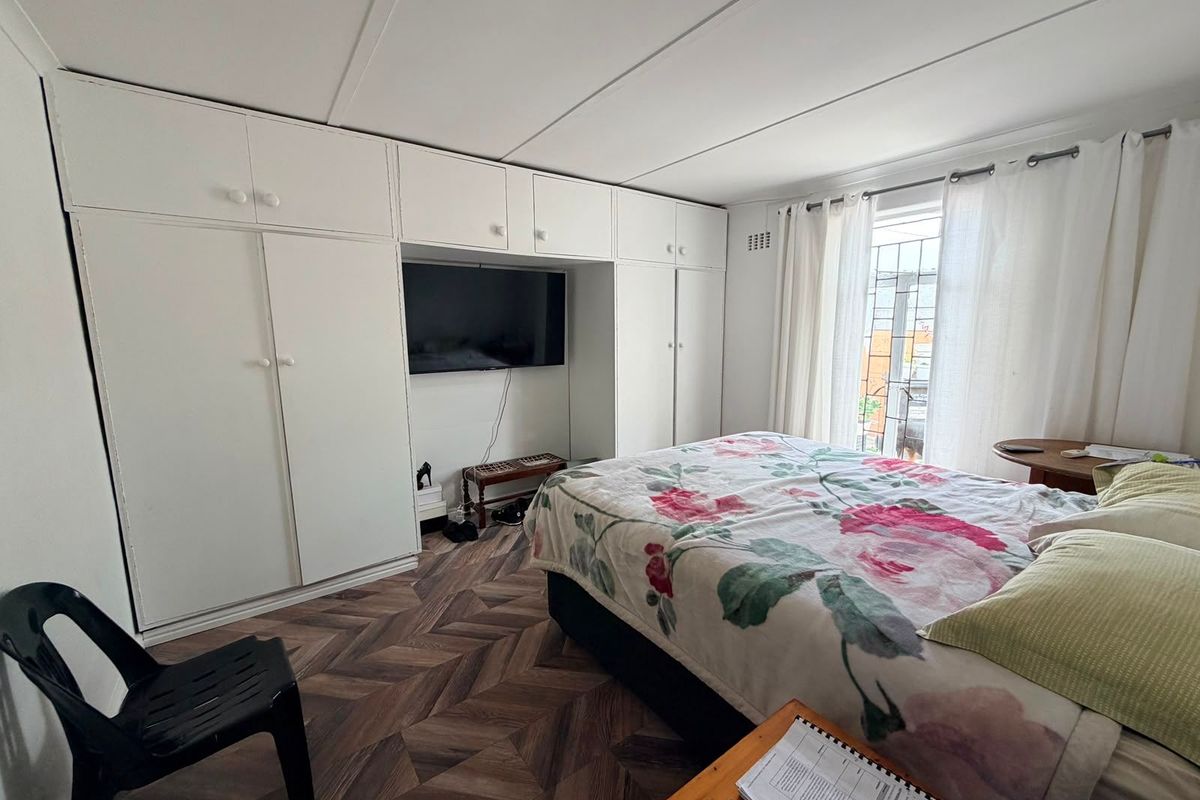 A bedroom featuring extensive built-in white cabinetry, herringbone-patterned flooring, and natural light through a window with security bars.