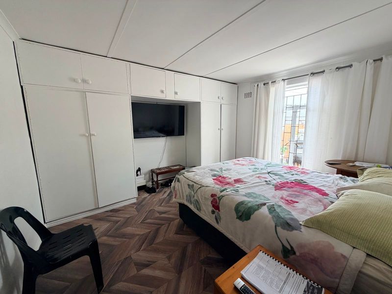 A bedroom featuring extensive built-in white cabinetry, herringbone-patterned flooring, and natural light through a window with security bars.