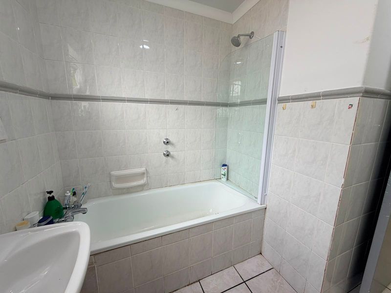 A functional bathroom featuring a built-in bathtub with a glass shower screen, tiled walls, and a pedestal basin.