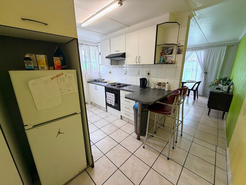 A functional kitchen featuring built-in cabinetry, an electric hob with extractor fan, tiled flooring, and a breakfast counter area.