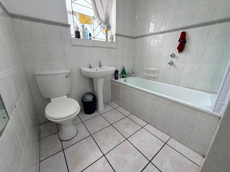 A functional bathroom featuring a pedestal basin, toilet, and bathtub with full-height wall tiling and tiled flooring.