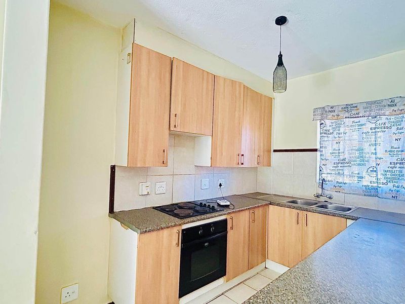 A functional kitchen featuring light wood-tone cabinetry, granite countertops, a built-in oven, electric hob, and tiled flooring with a neutral backsplash.