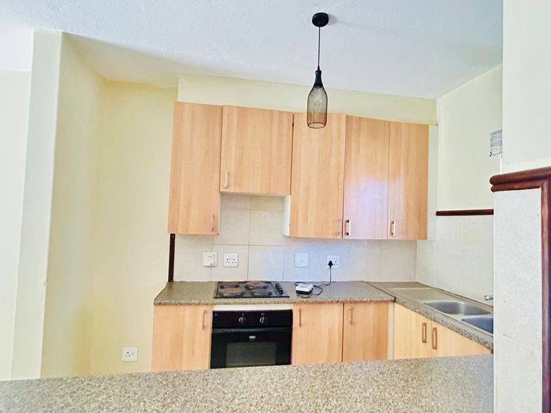 A functional kitchen featuring light wood-finish cabinetry, granite-look laminate countertops, a built-in oven and hob, and a stainless steel sink.