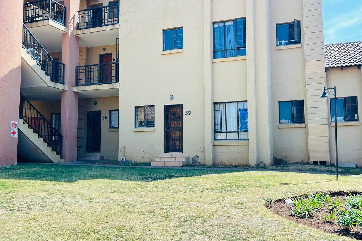 Exterior view of a multi-story apartment complex featuring balconies, a communal lawn, and external staircases with security gates.