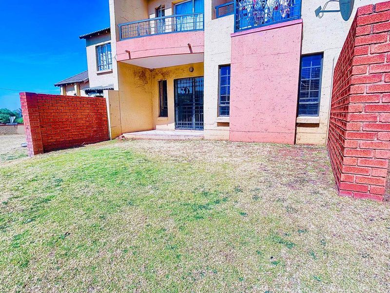 Rear view of the apartment building featuring a private garden, brick boundary walls, and upper-level balconies with metal railings.