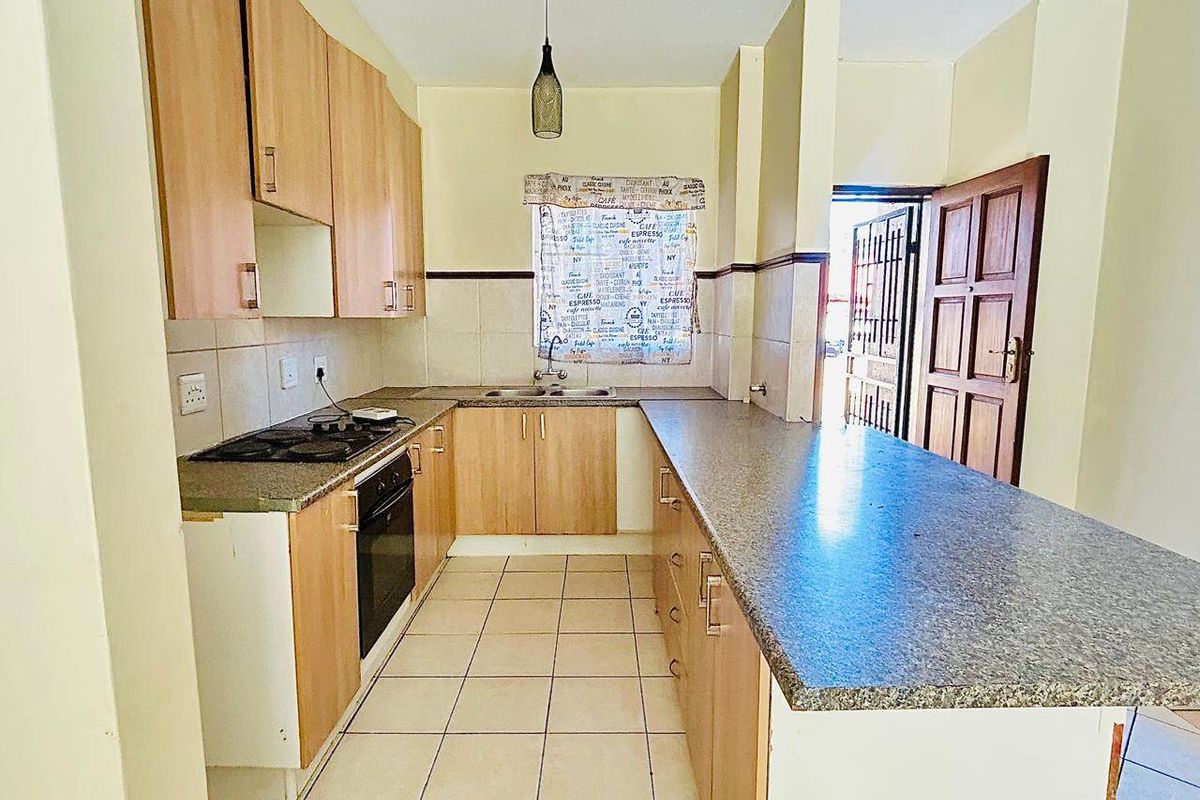 A functional kitchen featuring light wood cabinetry, laminate countertops, built-in oven and hob, and tiled flooring with a breakfast bar area.