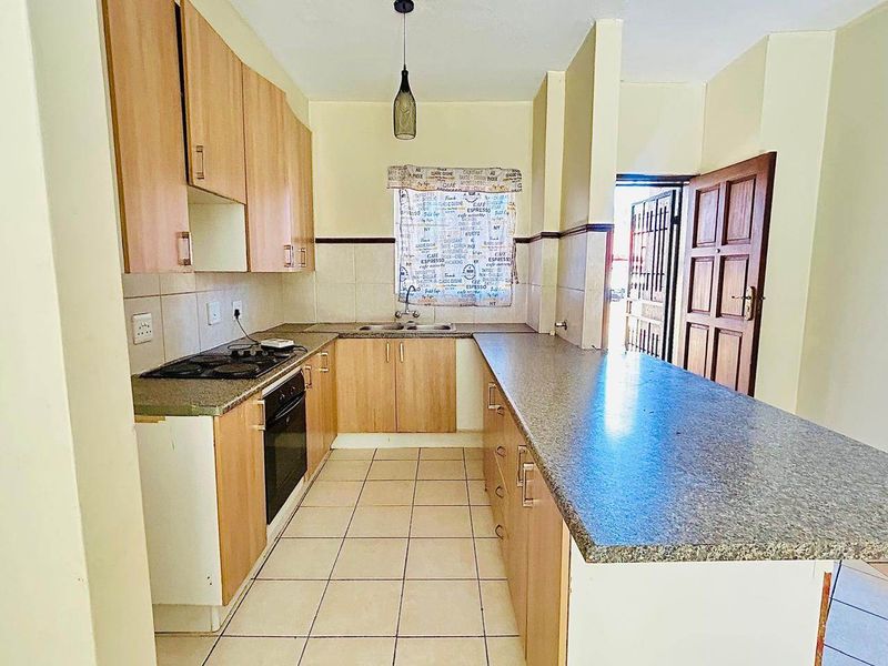 A functional kitchen featuring light wood cabinetry, laminate countertops, built-in oven and hob, and tiled flooring with a breakfast bar area.