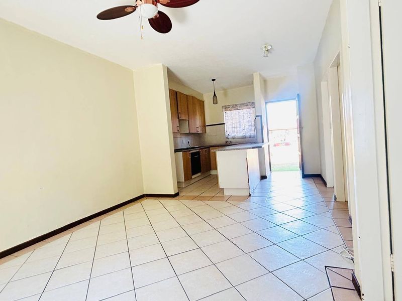 An open-plan living and kitchen area featuring tiled flooring, a ceiling fan, and functional built-in kitchen cabinetry with an island.
