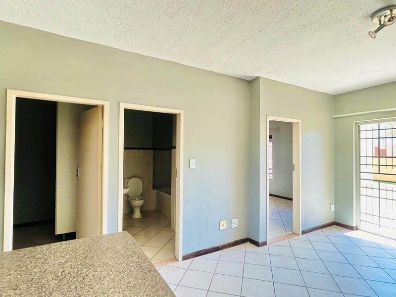 An open-plan living area featuring tiled flooring, a built-in counter, and access to adjacent rooms and a secure exterior door.