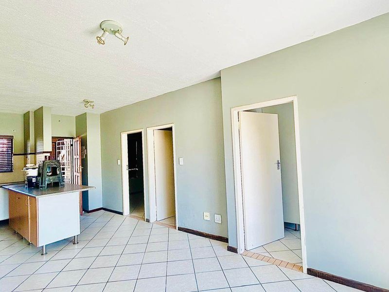 An open-plan living and kitchen area featuring tiled flooring, a central kitchen island, and multiple internal doorways leading to other rooms.