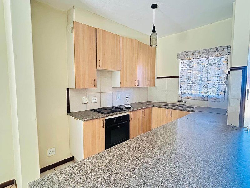 Functional kitchen featuring light wood-look cabinetry, granite-style laminate countertops, built-in oven, electric hob, and a double stainless steel sink with tiled backsplash.