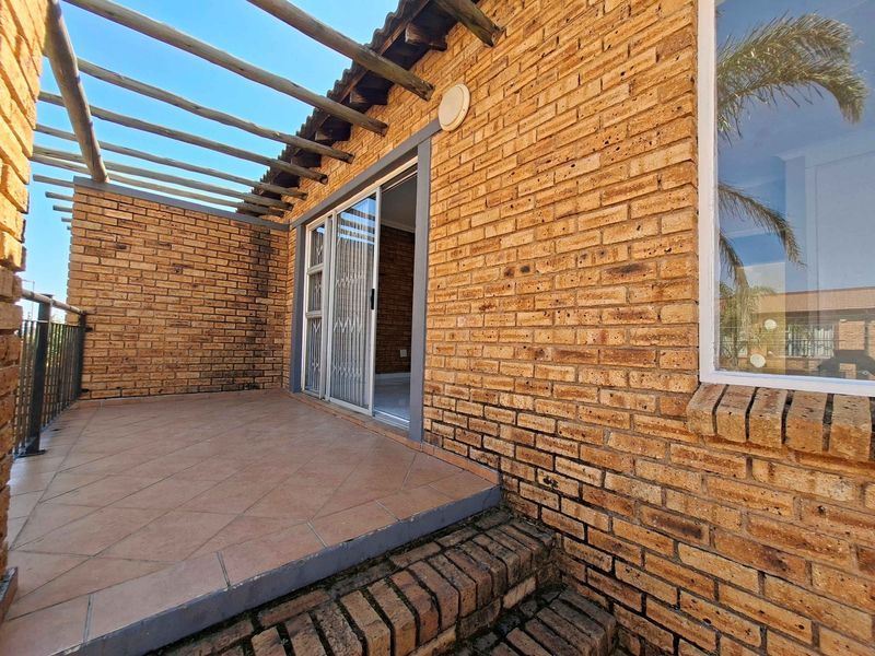 A covered outdoor patio featuring exposed brick walls, tiled flooring, and a timber pergola, providing a functional space for outdoor relaxation.