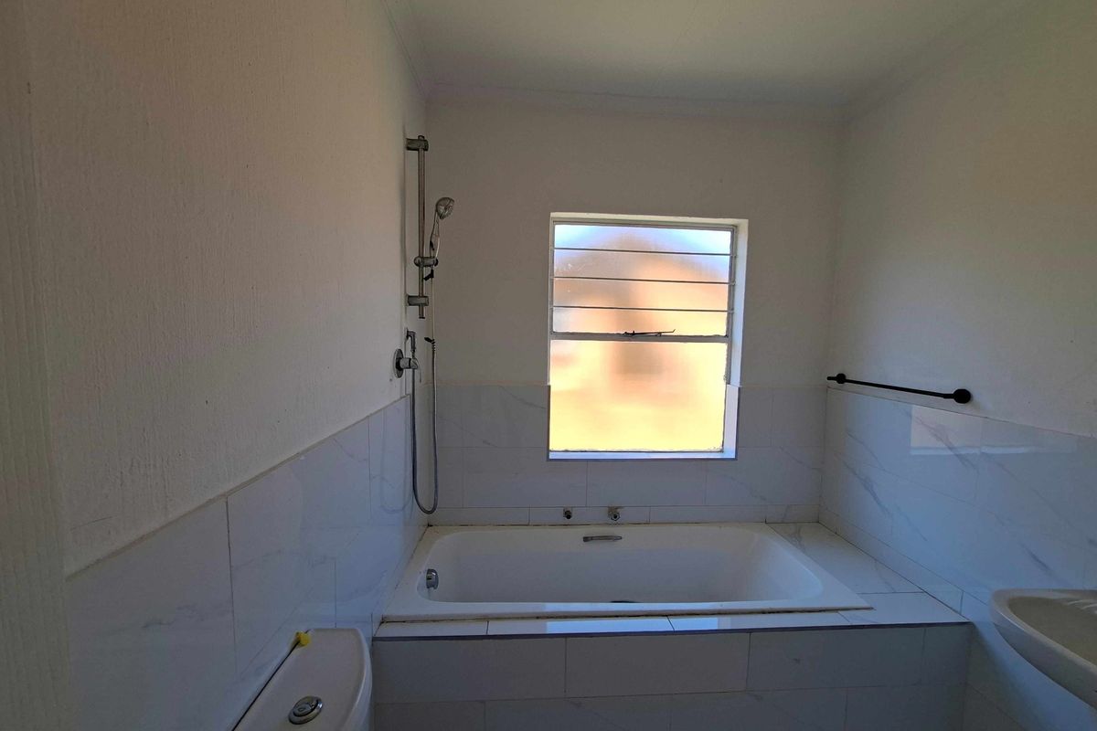 A functional bathroom featuring a built-in bathtub with shower attachment, a wall-mounted basin, and a toilet, finished with white wall tiles.