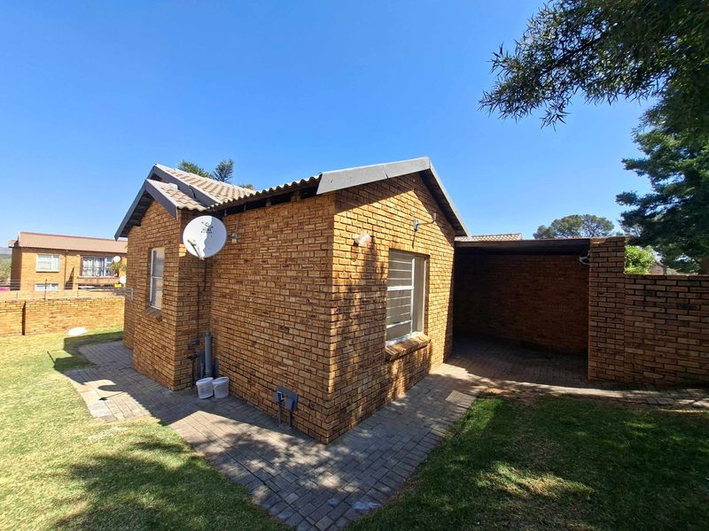 Rear view of a face brick townhouse featuring a covered patio area, paved walkways, and a small surrounding garden.
