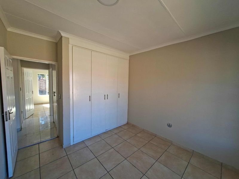 A bright, empty bedroom featuring neutral tiled flooring, built-in cupboards, and a coved ceiling, offering a clean canvas for personalization.