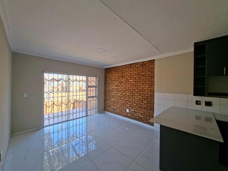 An open-plan living area featuring polished tiled floors, an exposed brick feature wall, and a sliding door leading to the exterior.