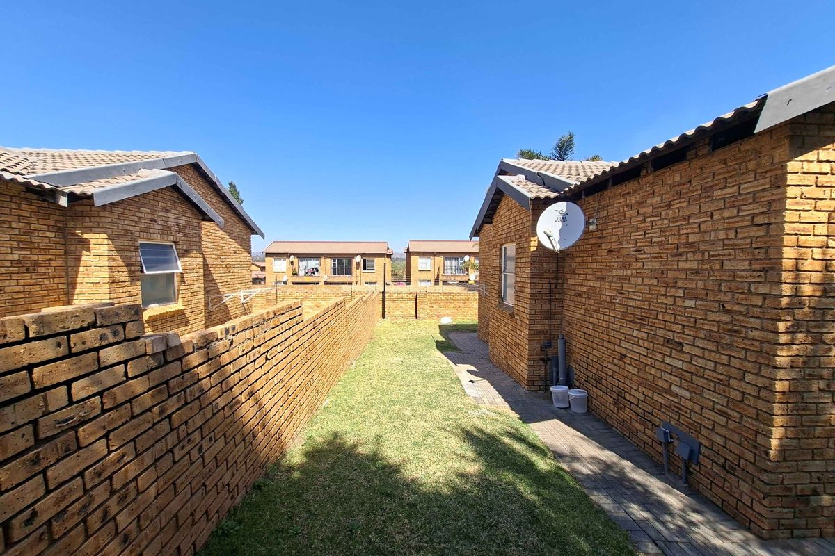 A rear exterior view of a townhouse complex featuring face brick construction, a small private lawn, and a paved walkway between units.