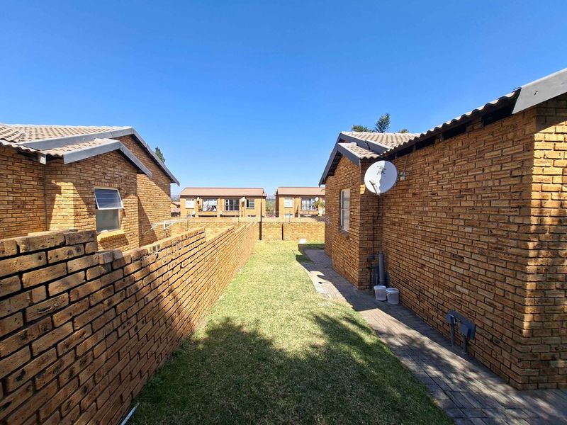 A rear exterior view of a townhouse complex featuring face brick construction, a small private lawn, and a paved walkway between units.