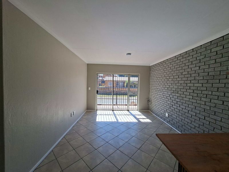 An empty living room featuring tiled flooring, an exposed brick feature wall, and a sliding glass door with a security gate leading outside.