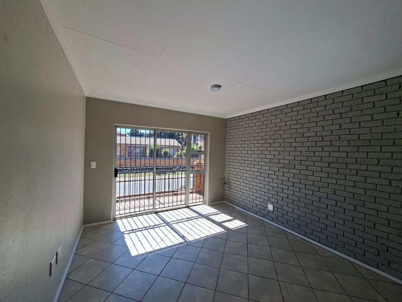 An empty living room featuring tiled flooring, a grey exposed brick feature wall, and a sliding glass door with an integrated security gate.