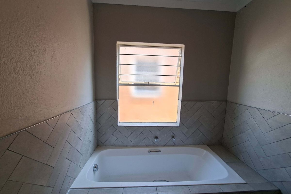 A clean bathroom featuring a built-in bathtub with stylish herringbone tiled surround and a window with security bars.