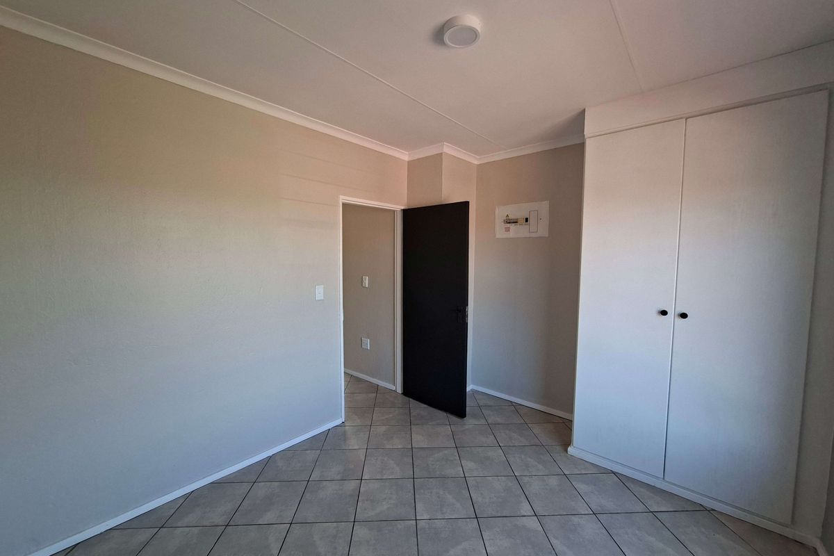 A clean, empty bedroom featuring neutral wall tones, tiled flooring, and a built-in wardrobe, offering a versatile space ready for personalization.