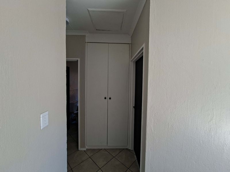 A functional hallway featuring tiled flooring and a built-in storage cupboard, providing access to adjacent rooms within the apartment.