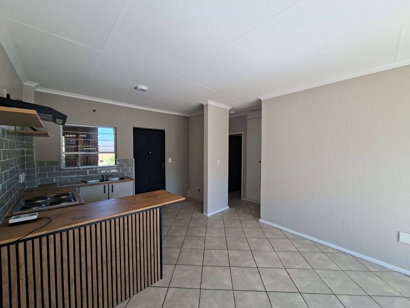 An open-plan kitchen and living area featuring tiled floors, modern cabinetry, a breakfast bar, and a neutral color palette, presenting a clean, vacant space.