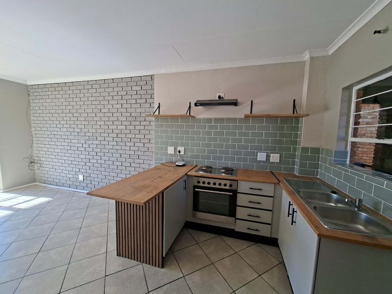 Modern kitchen featuring a built-in oven, electric hob, subway tile backsplash, wooden countertops, and a stylish slatted wood breakfast bar.