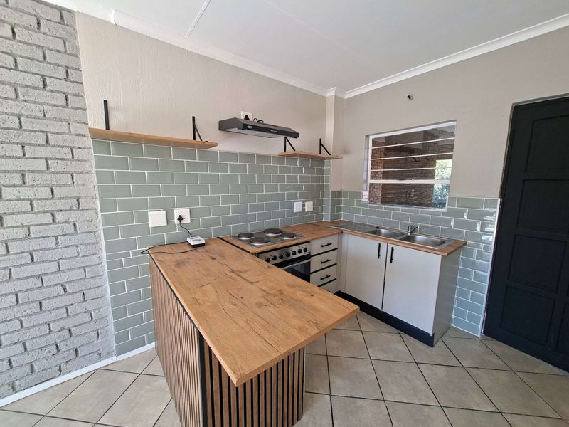 Modern kitchen featuring a subway tile backsplash, timber-look countertops, built-in oven with hob, extractor fan, and an exposed brick feature wall.