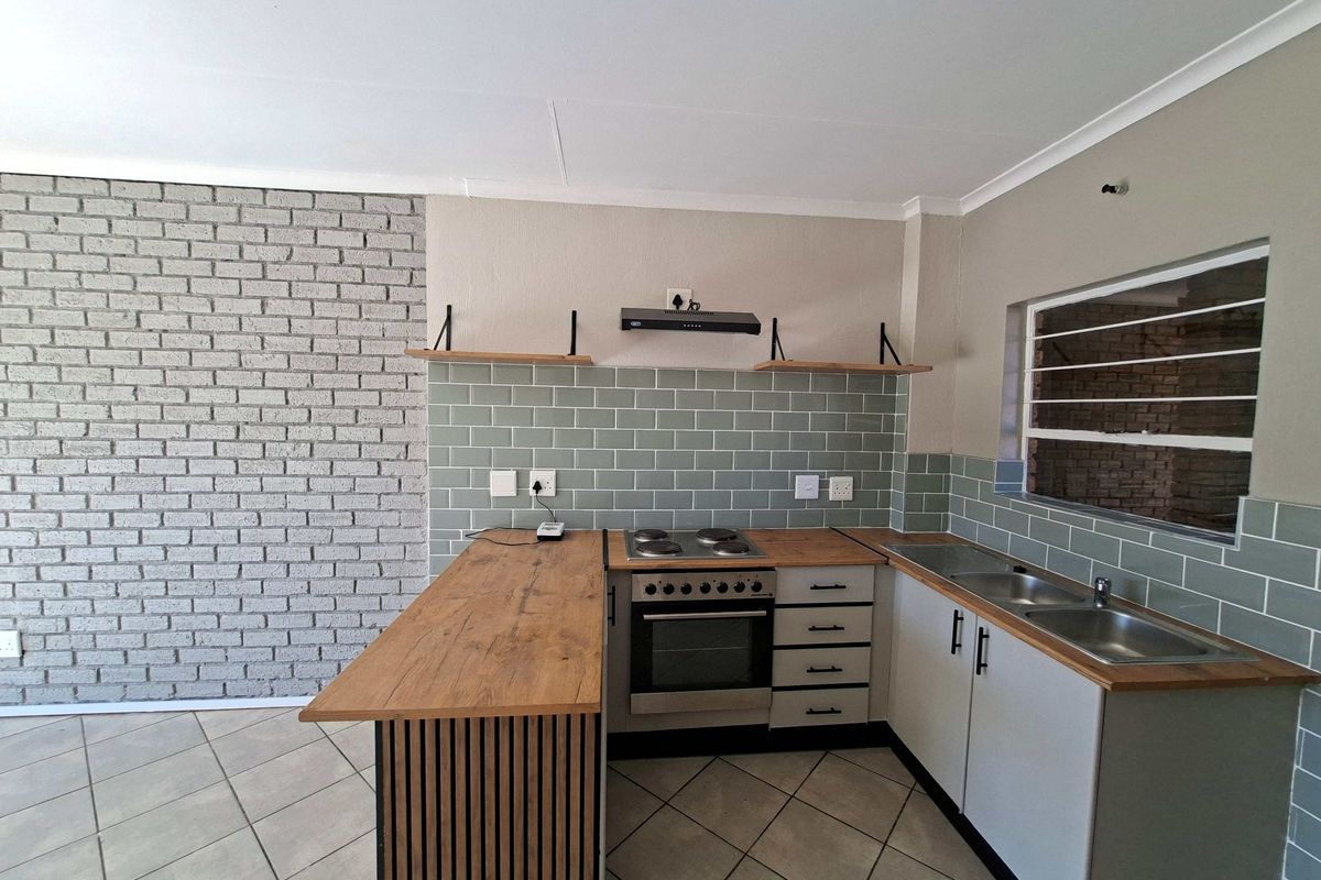 Modern kitchen featuring a brick accent wall, subway tile backsplash, wooden countertops, built-in oven with hob, and ample cabinetry.