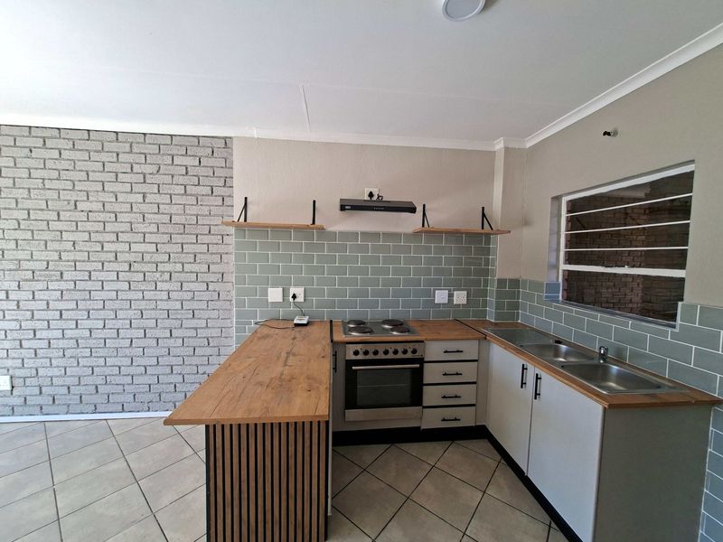 Modern kitchen featuring a brick accent wall, subway tile backsplash, wooden countertops, built-in oven with hob, and ample cabinetry.