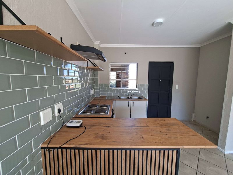 Modern kitchen featuring a subway tile backsplash, wooden countertops, electric hob, extractor fan, and a functional island with slatted detailing.