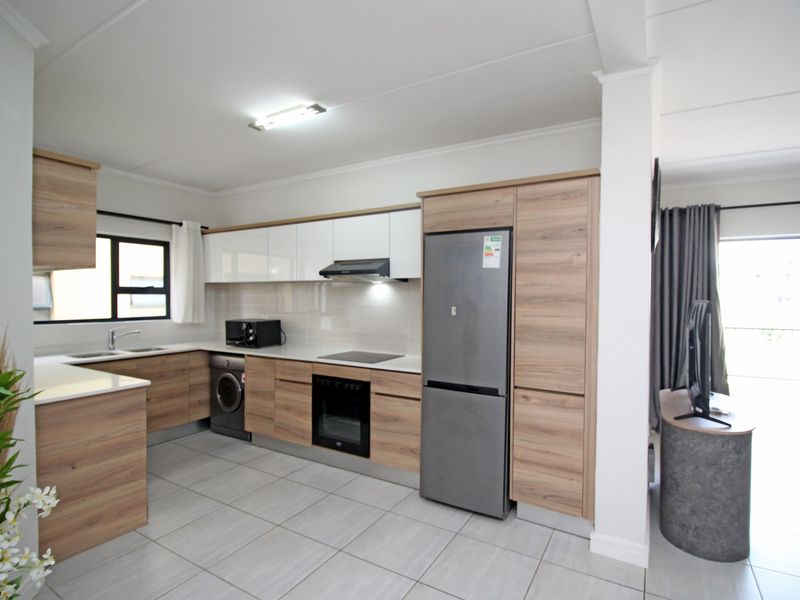 Modern open-plan kitchen featuring wood-grain and white cabinetry, stone countertops, integrated appliances, and neutral tiled flooring, seamlessly connecting to the living area.