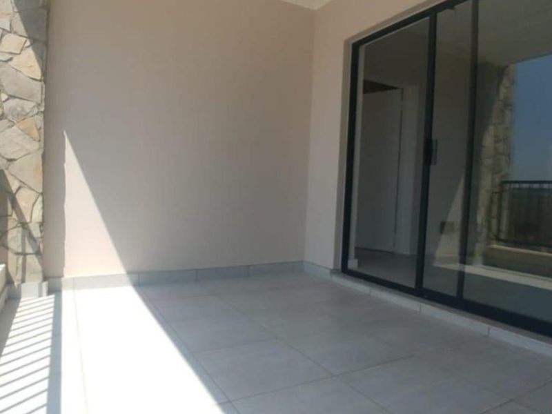 A clean, empty balcony featuring tiled flooring, a stone-clad pillar, and a sliding glass door providing access to the interior.