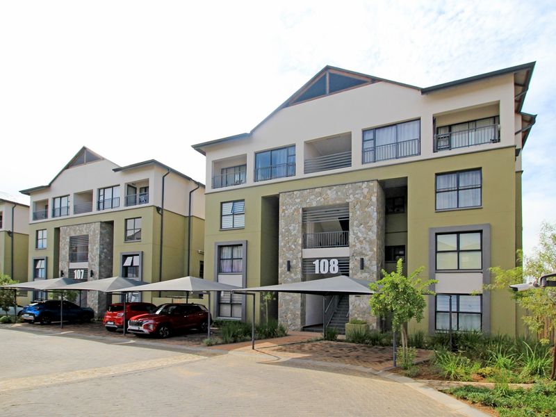 Front elevation of a modern multi-story apartment complex featuring stone facade accents, private balconies, and dedicated covered parking bays.