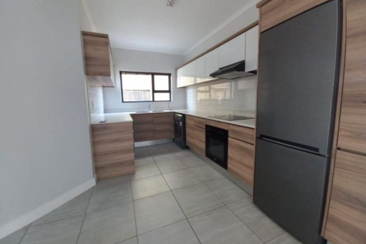 Modern kitchen featuring wood-grain cabinetry, white countertops, tiled backsplash, and integrated appliances including an oven and hob.