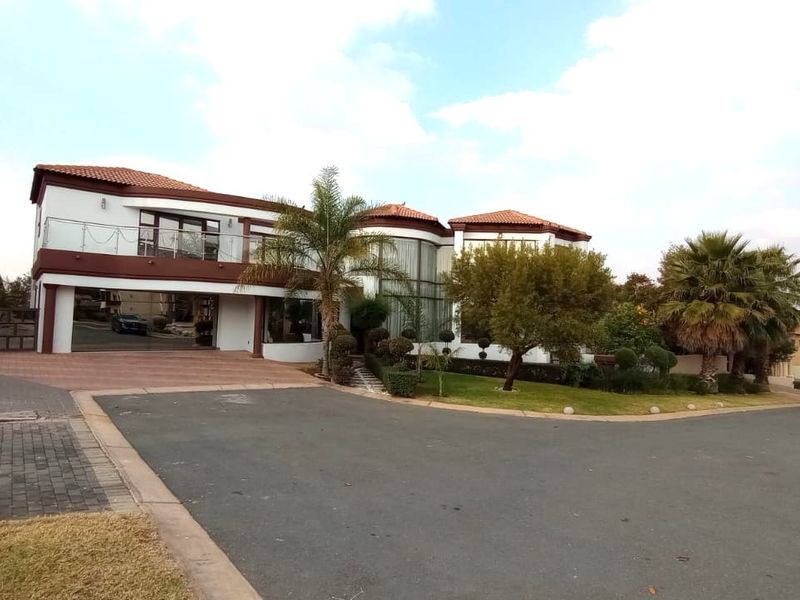 A well-maintained double-storey residential property featuring a paved driveway, landscaped garden, and a prominent balcony with glass railings.
