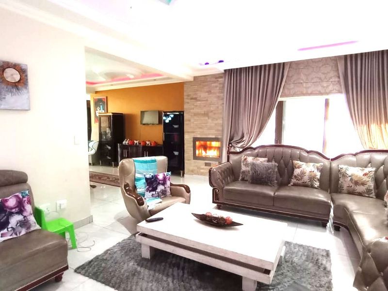 Spacious living room featuring a stone-clad fireplace, recessed ceiling lighting, and tiled flooring, creating a warm and inviting atmosphere.