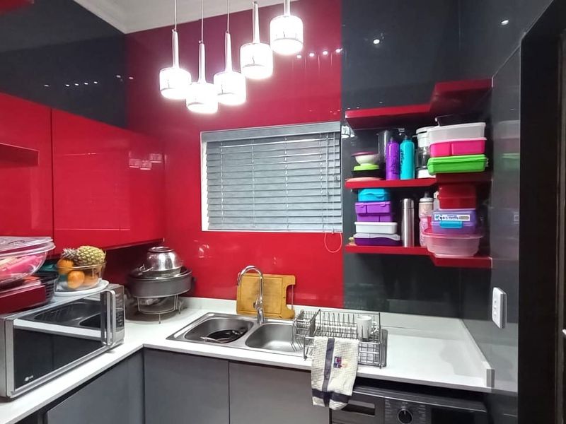 Modern kitchen featuring high-gloss red and grey cabinetry, stone countertops, a double basin sink, and contemporary pendant lighting.